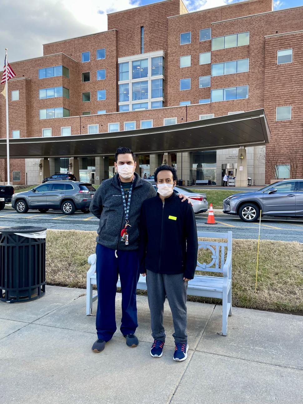 El doctor Juan Carlos Fierro Pineda, médico del NCI, posa junto a Gabriel, uno de sus pacientes, frente al Centro Clínico de los NIH en Bethesda, Maryland.