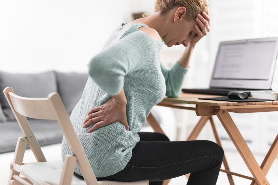 Person sitting while holding her back and head in pain