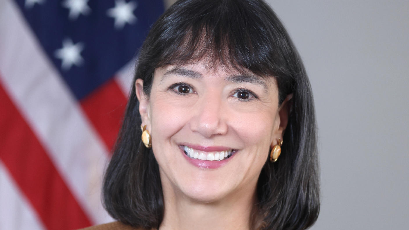 Woman (NCI Director Dr. Monica Bertagnolli) with dark hair wears a brown jacket over a patterned top and smiles at the camera.