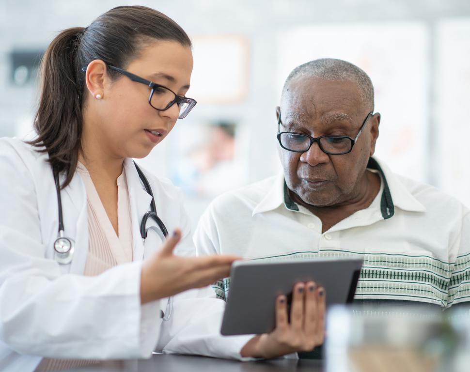 A young female doctor shows information on a tablet computer to an older black male patient.