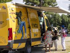 A brightly decorated van with a health care working speaking to several people from the van's side door.