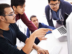 Four young men around a computer monitor
