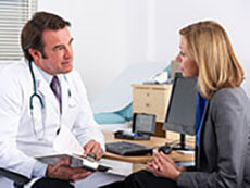 Female patient speaking with a male doctor sitting at a desk.