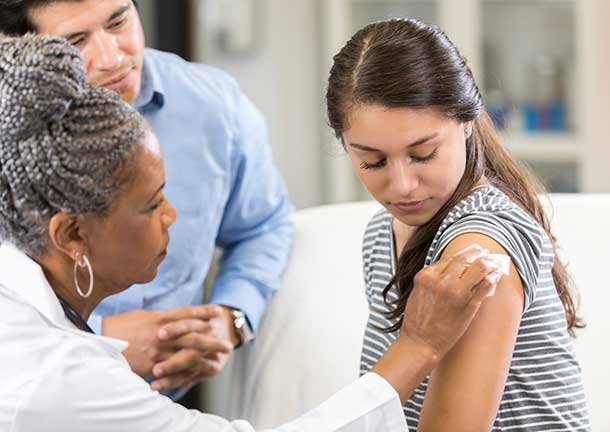 A teenage girl receiving a vaccine from a nurse.