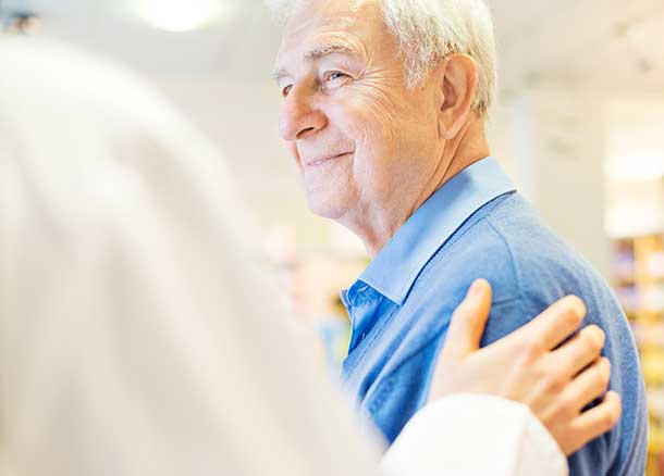 A doctor puts his hand on an older man's shoulder.