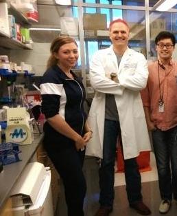 Ken Scott, wearing a white lab coat and smiling for photo with lab members Caitlin Grzeskowiak and Samuel Tsang
