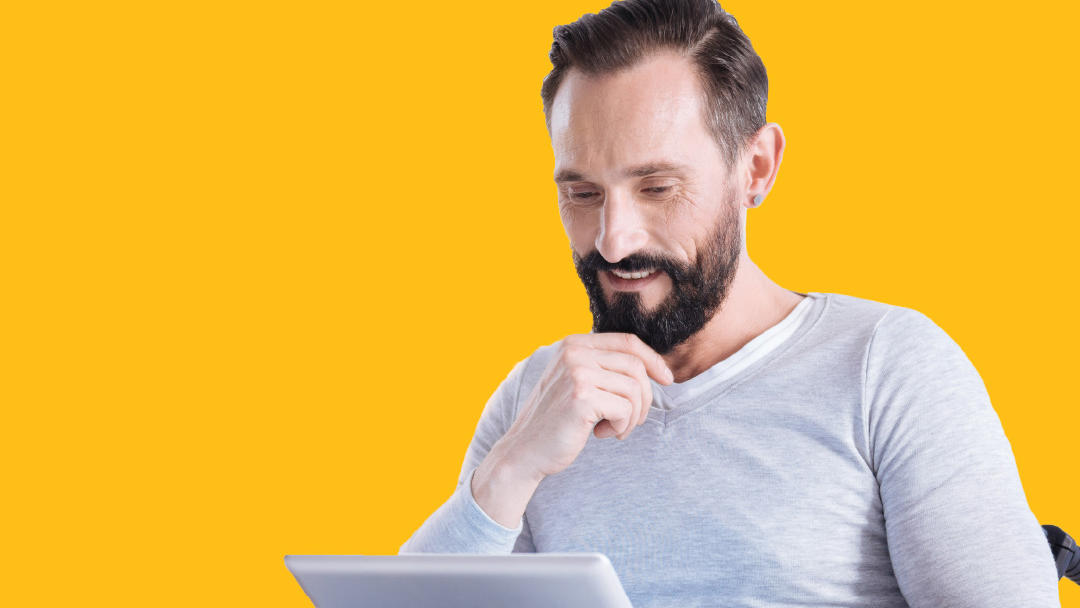 Man sitting in wheelchair looking at a tablet computer. 
