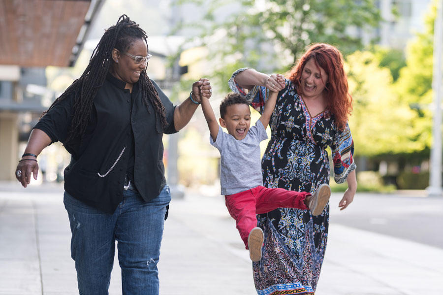 Two women who are a couple are swinging a child held between them and smiling