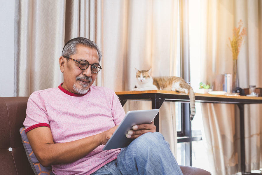 A man is sitting on a couch and looking at information on a tablet