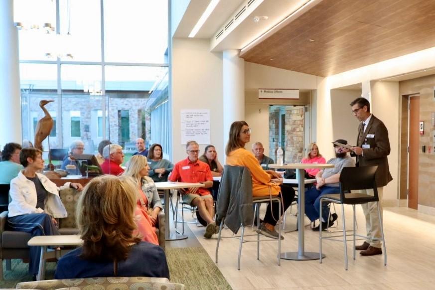 Investigador Principal del estudio en la Clínica Marshfield, Dr. Bob Greenlee, hablando al frente de la sala, presentando el chat de investigación a los asistentes del evento, entorno profesional de presentación, participación del público, discusión académica.