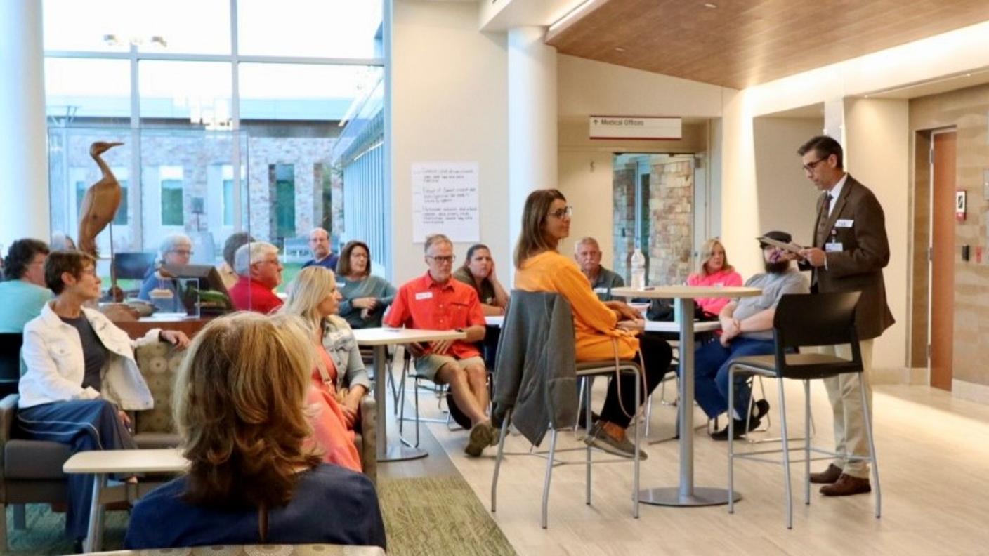 Study Principal Investigator at Marshfield Clinic, Dr. Robert Greenlee, speaking at the front of the room, introducing the research chat to event attendees, professional presentation setting, audience engagement, academic research discussion.