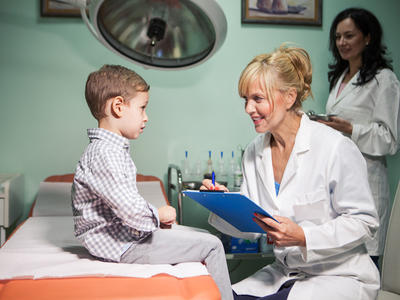 A doctor talks to a small boy who sits on a hospital bed