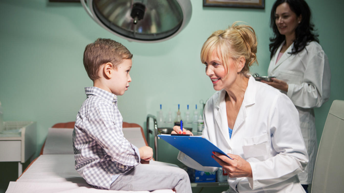 A doctor talks to a small boy who sits on a hospital bed