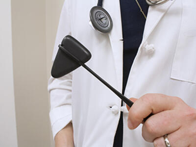 Person wearing lab coat holding a reflex hammer tool