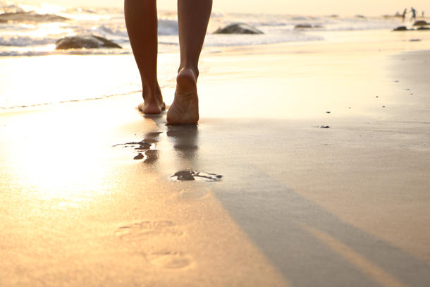 A close-up of feet walking on the beach at sunset