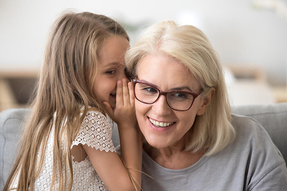 A little girl whispering in her grandma's ear