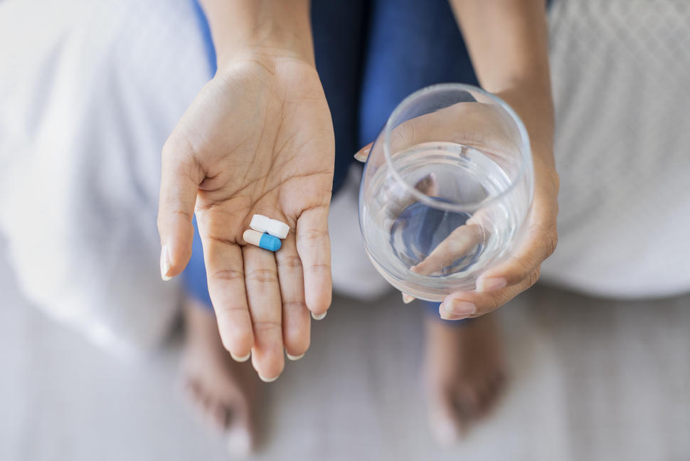 Hand holding two different pills and holding glass of water in the other hand