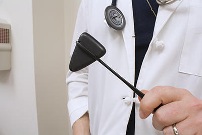 Person wearing lab coat holding a reflex hammer tool