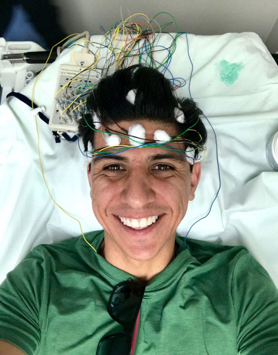 Julio in a hospital bed smiling with wires on his head