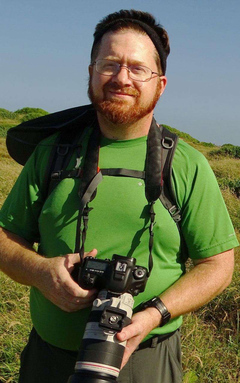 Steve outside in a field holding a camera with a very large lens