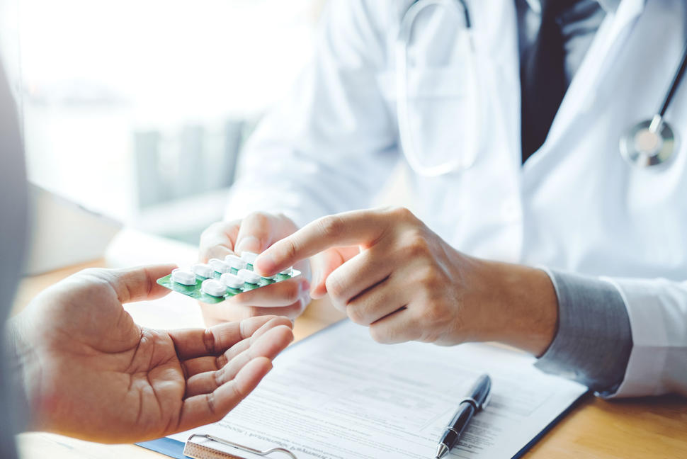 Doctor wearing a white coat handing out prescribed medication to a patient.