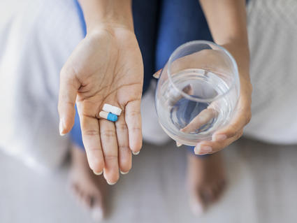 Hand holding two different pills and holding glass of water in the other hand