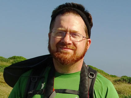 Steve outside in a field holding a camera with a very large lens