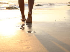 A close-up of feet walking on the beach at sunset
