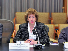 Patient advocate Kathy Oliver sitting at a table speaking into a microphone