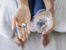 Hand holding two different pills and holding glass of water in the other hand