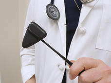 Person wearing lab coat holding a reflex hammer tool