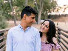 Liz and Julio smiling at one another while standing on a bridge during sunset