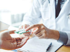 Doctor wearing a white coat handing out prescribed medication to a patient.