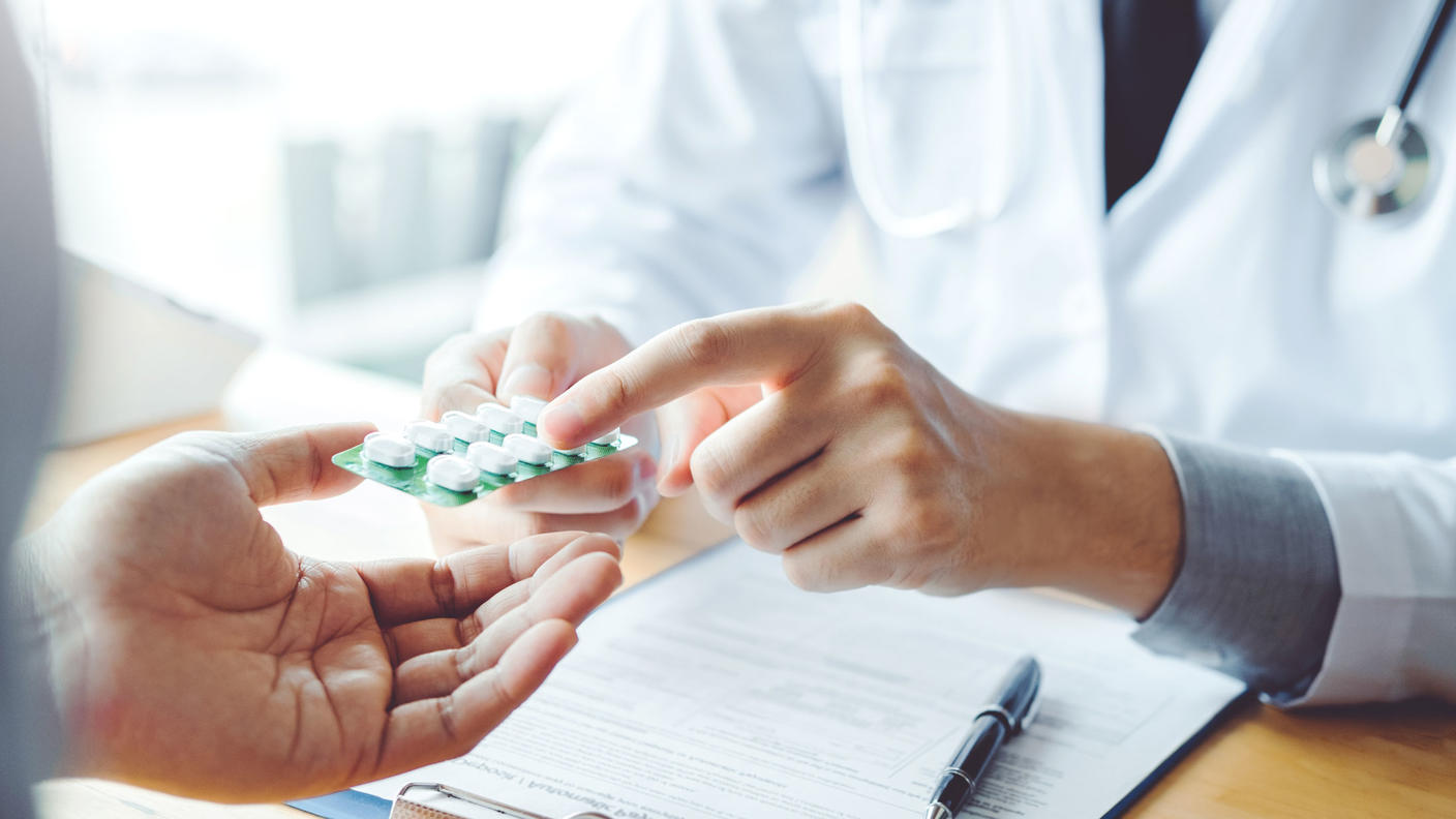 Doctor wearing a white coat handing out prescribed medication to a patient.