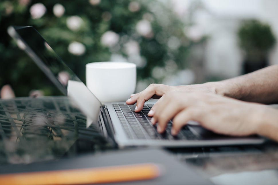 Close-up of hands typing on a laptop on a table outside