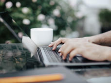 Close-up of hands typing on a laptop on a table outside