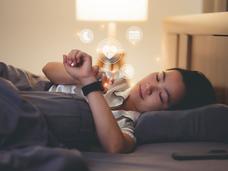 Woman lying in bed looking at her watch, which displays moon, heartbeat, calendar, and medical icons