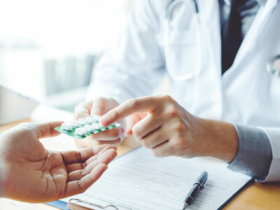 Doctor wearing a white coat handing out prescribed medication to a patient.
