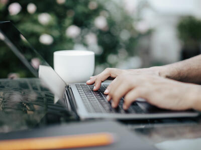 Close-up of hands typing on a laptop on a table outside
