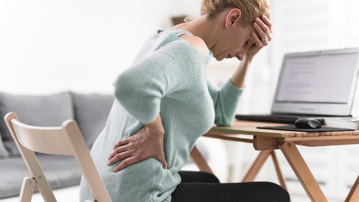 Person sitting while holding her back and head in pain