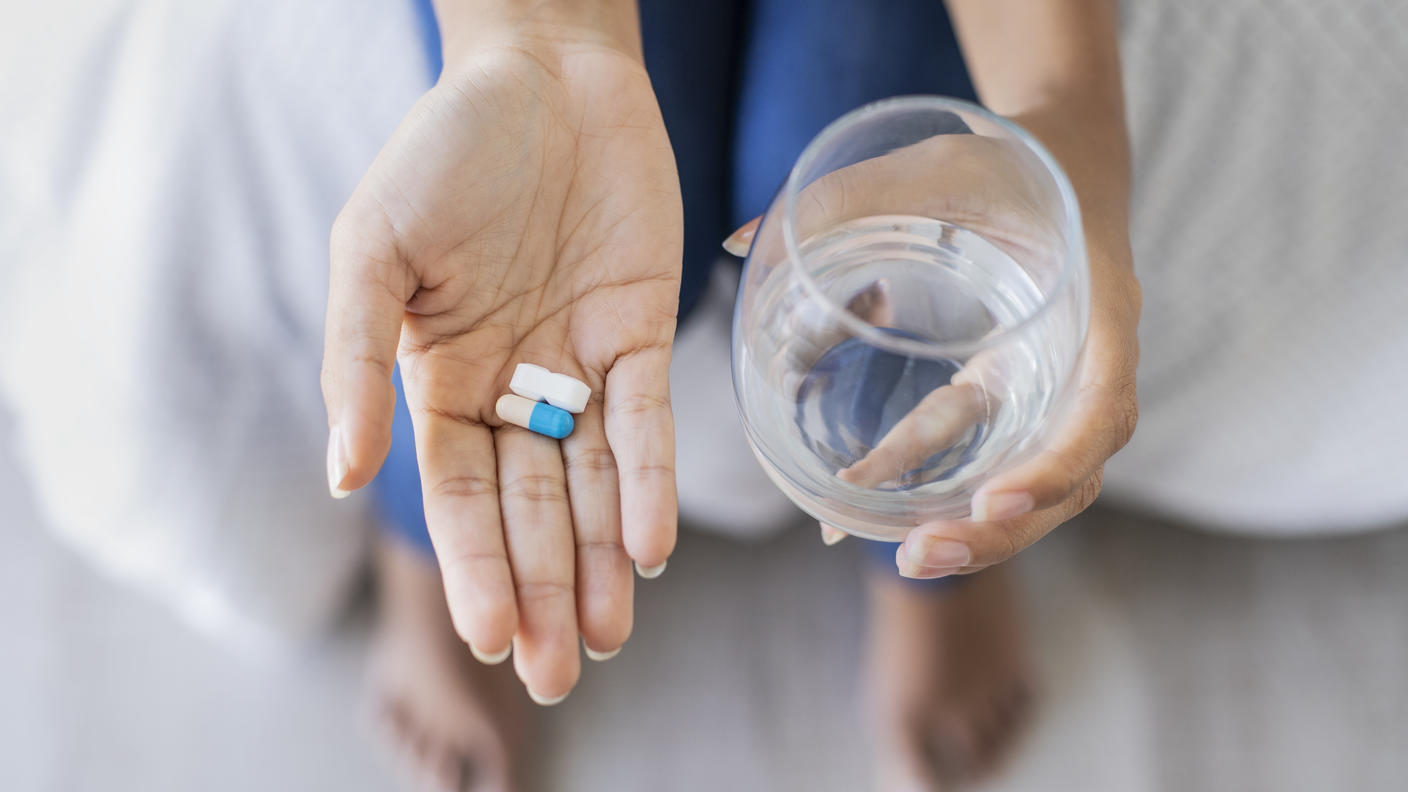 Hand holding two different pills and holding glass of water in the other hand