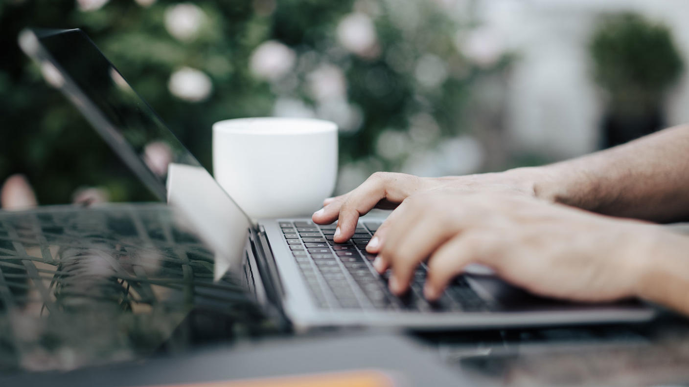 Close-up of hands typing on a laptop on a table outside