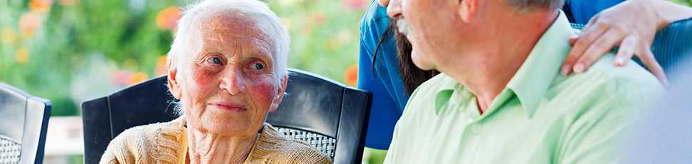 Elderly woman and man looking at each other outside with nurse.