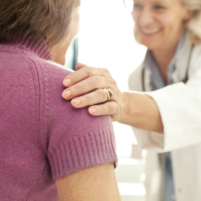 Una médica apoya la mano en el hombro de una paciente 