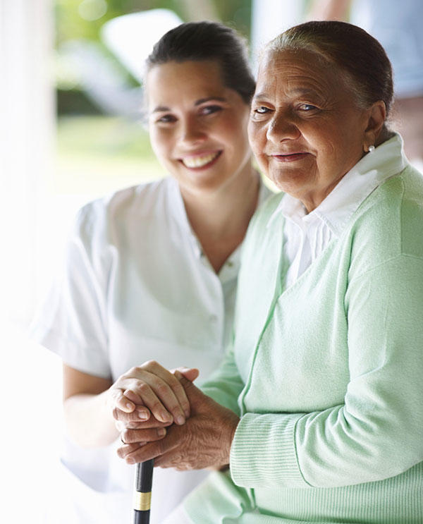 Older woman with cancer who is smiling, with her nurse, and holding a cane.  