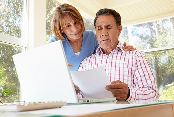 Un hombre y una mujer revisan documentos frente a una computadora.