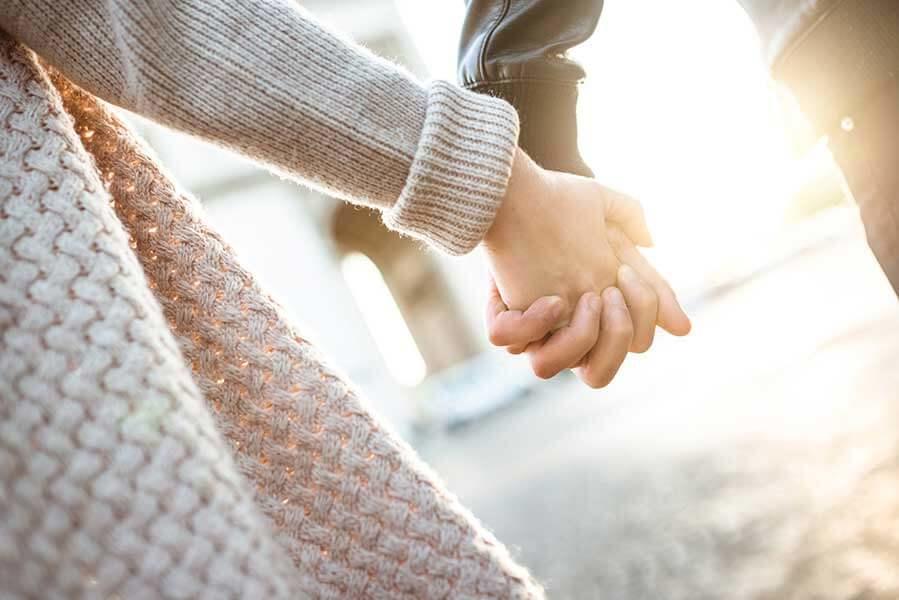 Man and woman holding hands as they walk in the sunshine.