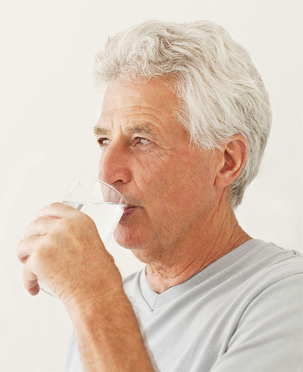 Older man who is drinking a full glass of water. 
