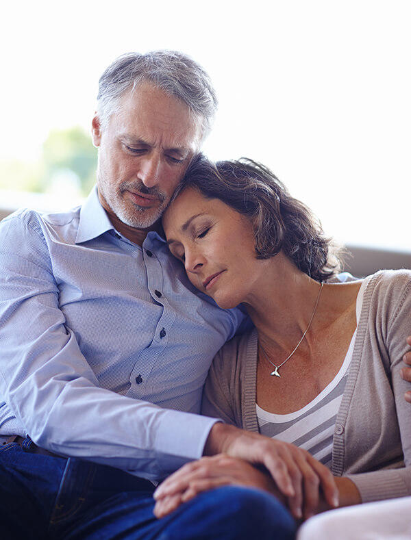 Woman seated beside man, eyes closed and leaning her head on his chest