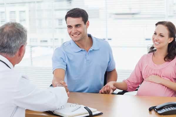 A pregnant person and their partner talking with a doctor at a desk.